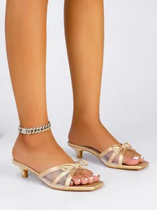 Detalle de sandalias doradas de tacón bajo con lazo y detalles de malla mesh.