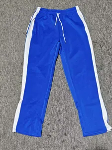 Blue side-button sports basketball pants with white stripes on a flat textured background