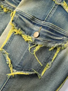 Macro detail showing the distressed denim jeans pocket with yellow fringe and a button