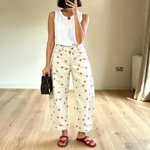 Full-length view of white barrel jeans with large pink polka dots and red sandals.