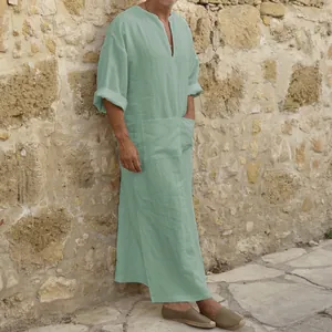 Side profile of a mint green men's cotton linen kaftan robe against a stone wall.
