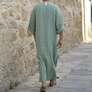 Back view of a relaxed sage green long cotton linen robe for men in a rustic alley