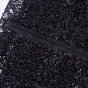 Detail van de zwarte lovertjes textuur en de nette paspelzak van de blazer.