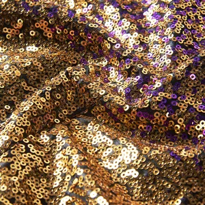 Detailopname van glinsterende gouden en paarse pailletten op de stof van een podiumkostuum