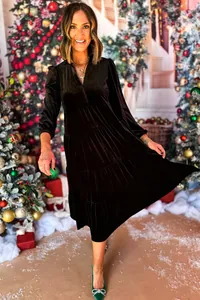 Modell trägt ein schwarzes Samtkleid mit V-Ausschnitt und Rüschen in Weihnachtsdekoration