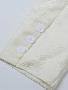 Detail close-up view of jacquard floral pattern and buttons on cream suit sleeve