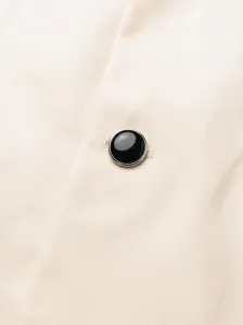 Macro view of a black polished button with silver rim on beige twill suit fabric