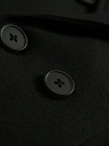Close-up of durable buttons and premium wool fabric on a men's black overcoat.