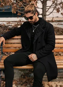 Stylish men's long black wool coat with plush collar shown on a model sitting on a bench.