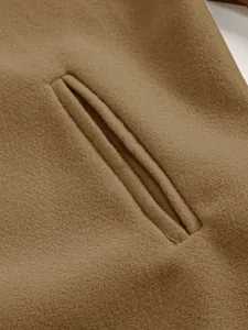 Close-up of welt pocket detail on brown woolen coat showing premium fabric texture