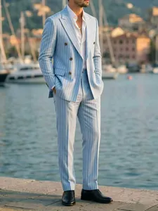 Full-body view of a stylish light blue pinstripe men's suit by the sea harbor.
