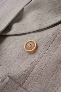 Macro detail of a resin button on a textured pinstriped beige business suit jacket