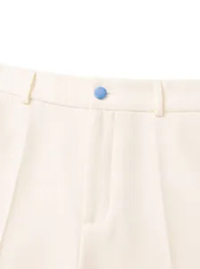 Detalle de la cintura de un pantalón de traje crema para hombre con botón azul