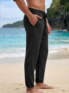 Detailed side view of men's black casual loose straight drawstring trousers on beach