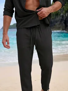Macro view of men's black linen drawstring trousers worn on a tropical beach resort
