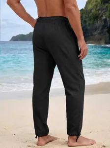 Relaxed back view of men's casual black linen-texture drawstring pants at the beach.