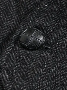 Close-up detail of a black leather-textured button on grey herringbone fabric vest