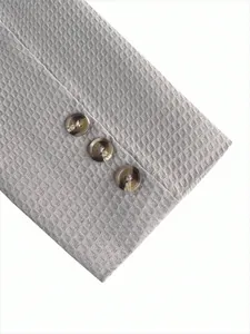 Detailopname van de manchet van een grijs getextureerd colbert met drie chique knopen