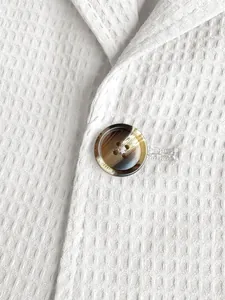 Macro-detail van witte wafelstructuur en decoratieve knoop op een heren blazer
