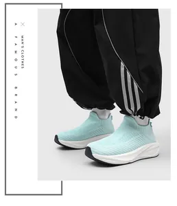 Detail view of mint green slip-on flyknit sock sneakers worn with black striped joggers