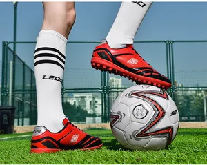 Detail von roten Turf-Fußballschuhen auf Kunstrasen mit einem Fußball im Spiel