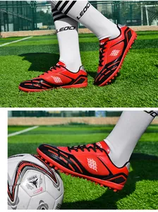 Professionelle rot-schwarze TF-Fußballschuhe für Kinder auf einem Kunstrasenplatz