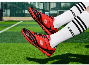 Detailansicht roter und schwarzer Fußballschuhe mit TF-Stollen auf Kunstrasenplatz