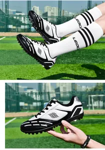 Detailansicht der schwarz-weißen TF-Fußballschuhe für Kinder auf einem Kunstrasenplatz.