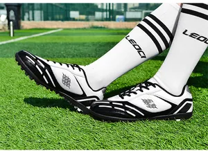 Professionelle schwarz-weiße Fußballschuhe mit TF-Stollen auf grünem Kunstrasen
