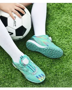 Close-up view of children's soccer shoes with rotary buckle and TF studs on green turf