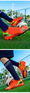 Close-up detail of orange soccer cleats with AG/FG spikes on green field