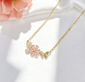 Dettaglio macro di una collana in acciaio titanio dorato con fiori di ciliegio rosa e farfalla
