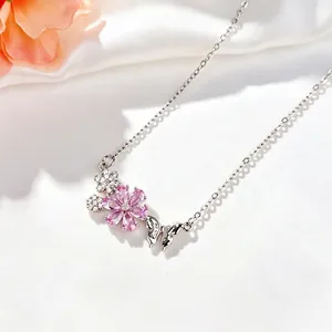 Primo piano del ciondolo con fiore di ciliegio rosa e farfalla su una collana d'argento.