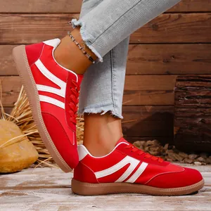 Red retro women's sneakers with white stripes shown on foot against wood background