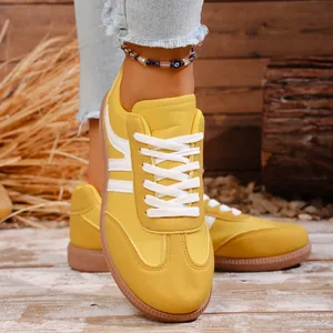 Detail shot of retro yellow flat sneakers featuring white laces and side stripe design