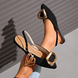 Close-up of black French pointed-toe flat sandals with decorative gold buckles.
