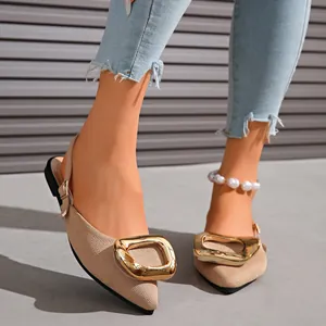 Detail view of beige pointed-toe flat sandals featuring a large decorative gold buckle