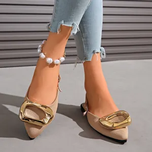 Detailed view of beige pointed toe flats with oversized gold buckle and pearl anklet