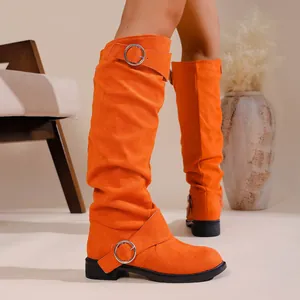 Close-up of bright orange suede slouchy knee-high boots with silver buckle
