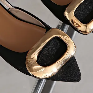 Close-up detail of black pointed-toe flats with a large gold buckle and glittery fabric.