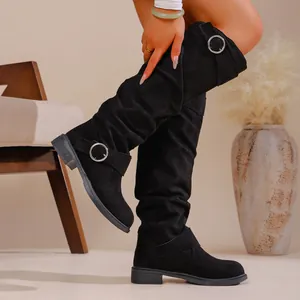 Close-up detail of black slouchy suede boots featuring stylish round metal buckle straps.