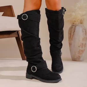 Close-up of black suede slouchy boots with decorative silver buckle straps on model's legs.