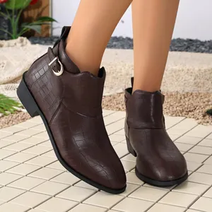 Close-up of brown crocodile texture ankle boots with buckle detail on a tiled patio