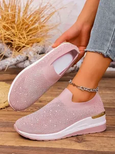 Close-up of pink flyknit wedge sneakers with sparkling rhinestone details and a gold accent.