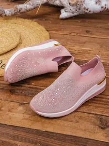 Close-up of pink fly-woven slip-on sneakers with sparkling rhinestone details and wedge sole