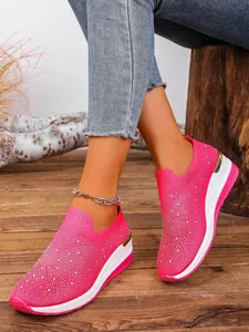 Detailed view of pink fly-knit wedge sneakers with rhinestone accents on a wearer