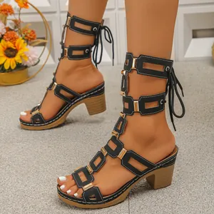 Detail view of black lace-up gladiator sandals with gold hardware on a model.