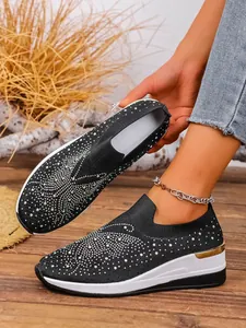 Close-up of black fly-knit wedge sneakers for women featuring sparkling rhinestone patterns.