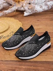 Close-up of black fly-knit wedge sneakers with sparkling rhinestone butterfly patterns.
