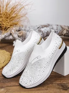 Detailed view of white fly-knit slip-on shoes featuring a sparkling rhinestone butterfly pattern